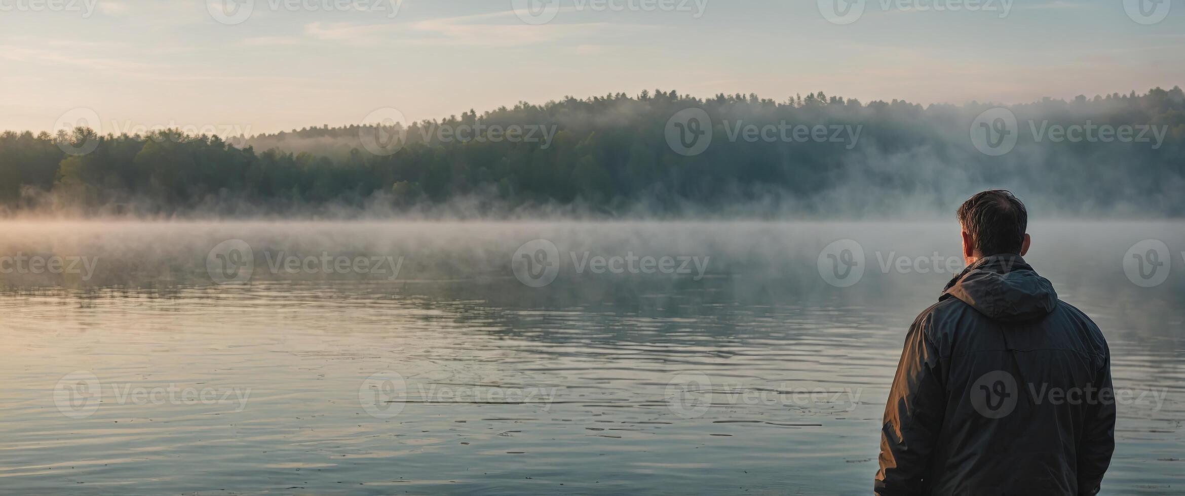 A man standing in front of a foggy lake preparing for his morning routine with a round of deep breaths. photo