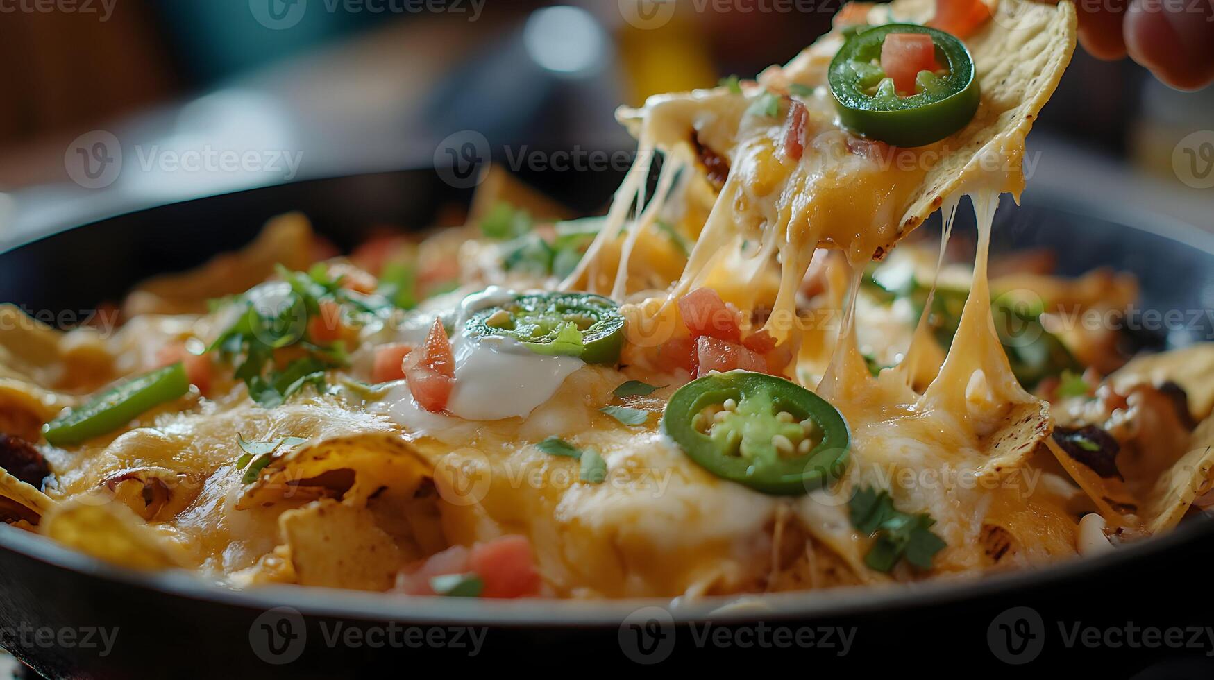 A hot skillet of nachos with cheese stretching between chips as someone lifts one out, the melted cheese glistening, with toppings like jalapenos, tomatoes, and sour cream photo