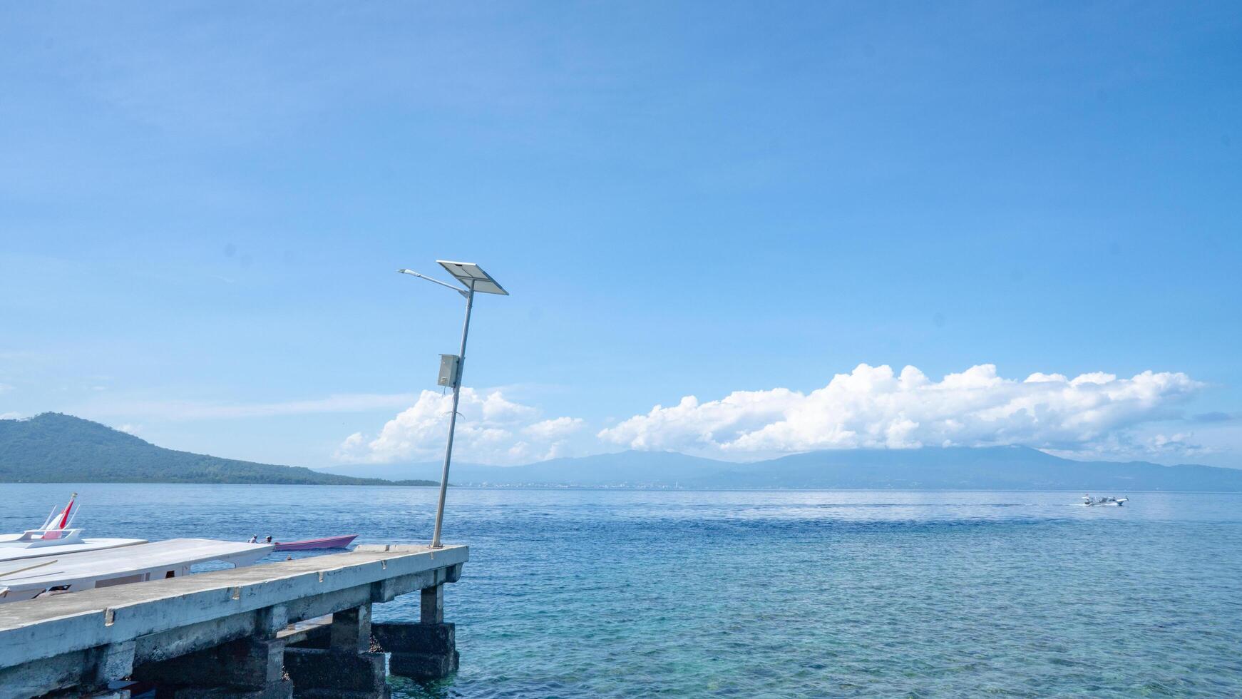 Tranquil Sea View From a Pier. A serene view of a pier extending into a tranquil sea, showcasing a clear blue sky with wispy clouds and a distant mountain range. photo