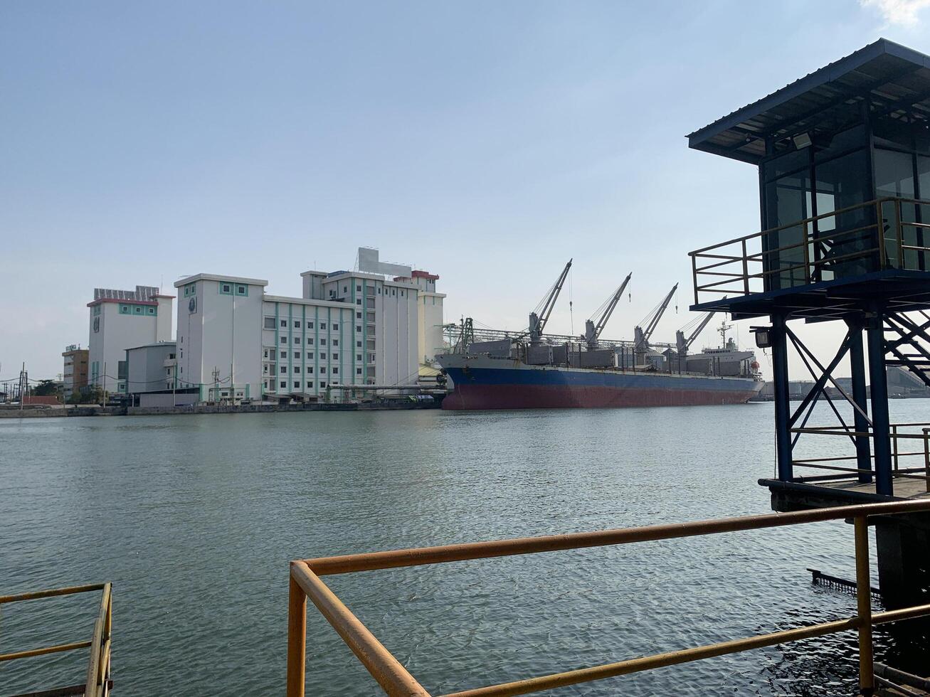 Cargo Ship Docked at a Port. A large cargo ship docked at a port, with several industrial buildings and cranes in the background. photo