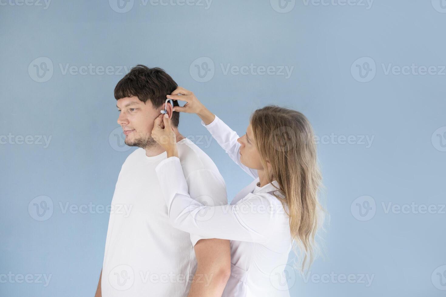 young male patient testing hearing aid in clinic exam room, female doctor helping photo