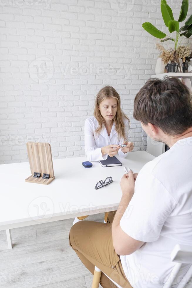 young male patient testing hearing aid in clinic exam room, female doctor helping photo