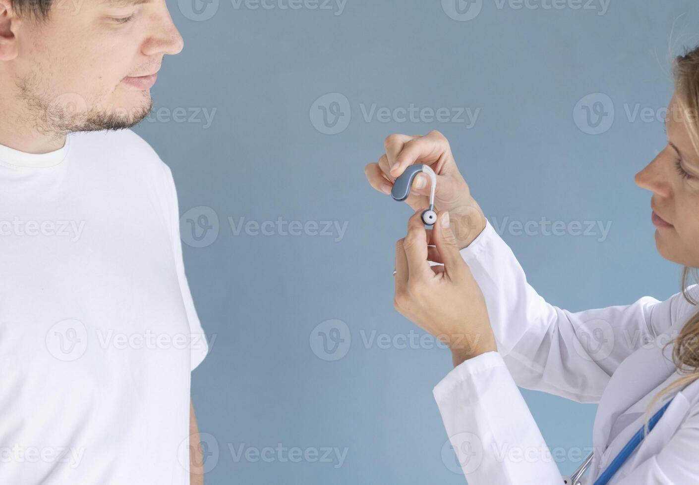 young male patient testing hearing aid in clinic exam room, female doctor helping photo