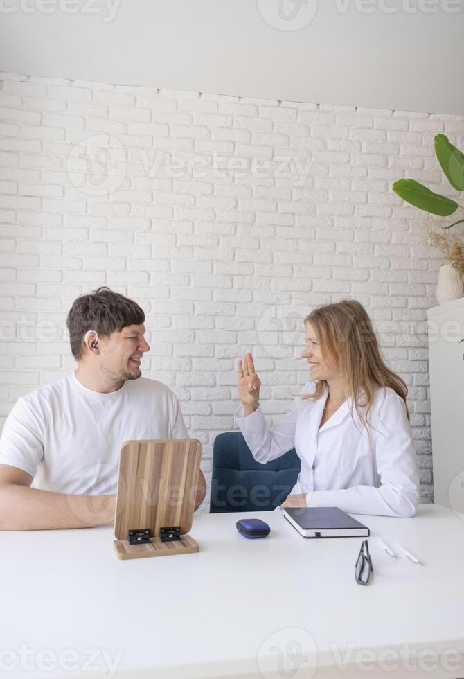 young male patient testing hearing aid in clinic exam room, female doctor helping photo