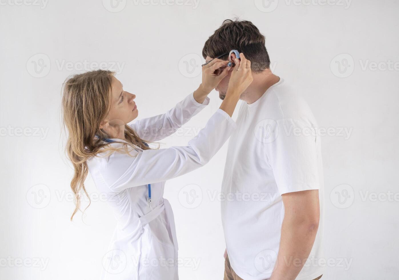 young male patient testing hearing aid in clinic exam room, female doctor helping photo
