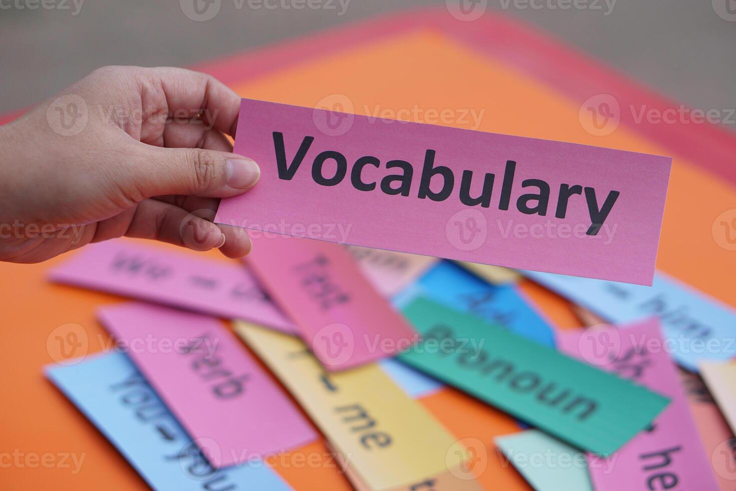 Close up hand holds paper card with text vocabulary. Concept, education, learning, studying language. Education. Reading and memorizing strategy of learning process lesson. photo