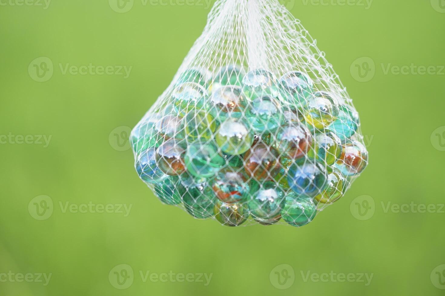 Close up net bag of marbles balls, small spherical object often made from glass. Green background. Concept. object use as toy for playing games or use for DIY craft decoration. photo