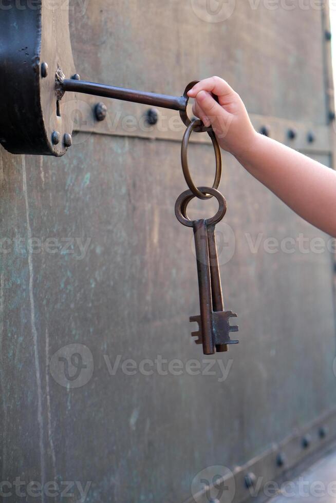 a small child's hand tries to open a padlock with a large key photo