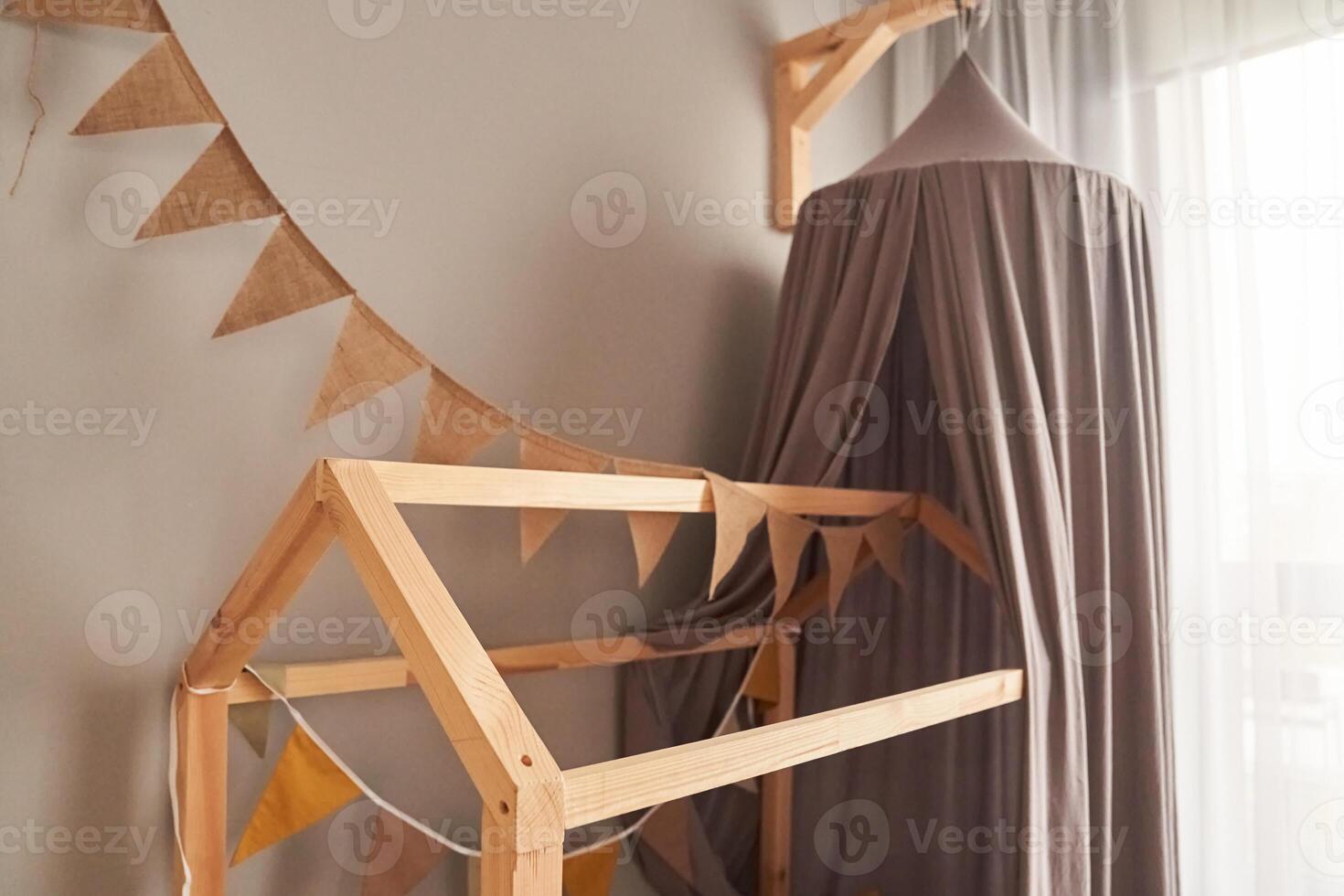 Decor in domestic, cosy, modern childrens bedroom with wooden bed like a house, with fabric canopy for children, brown party bunting flags. Background with copy space. Concept of interior design photo