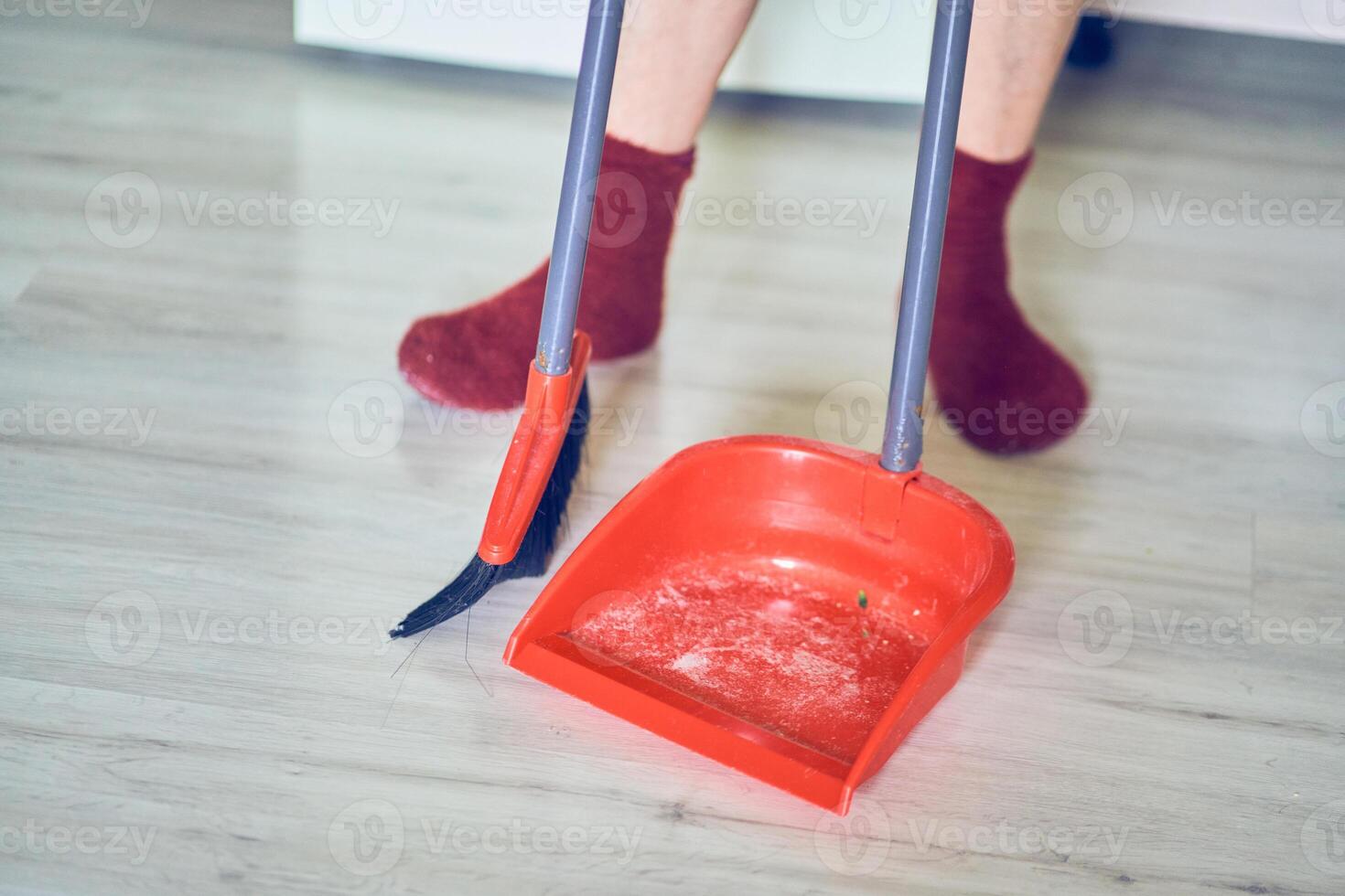 Close up of a plastic dustpan and red broom on the floor with unrecognisable woman, professional cleaner, worker with copy space. Concept of cleaning home, sweeping floor, cleaning dust photo