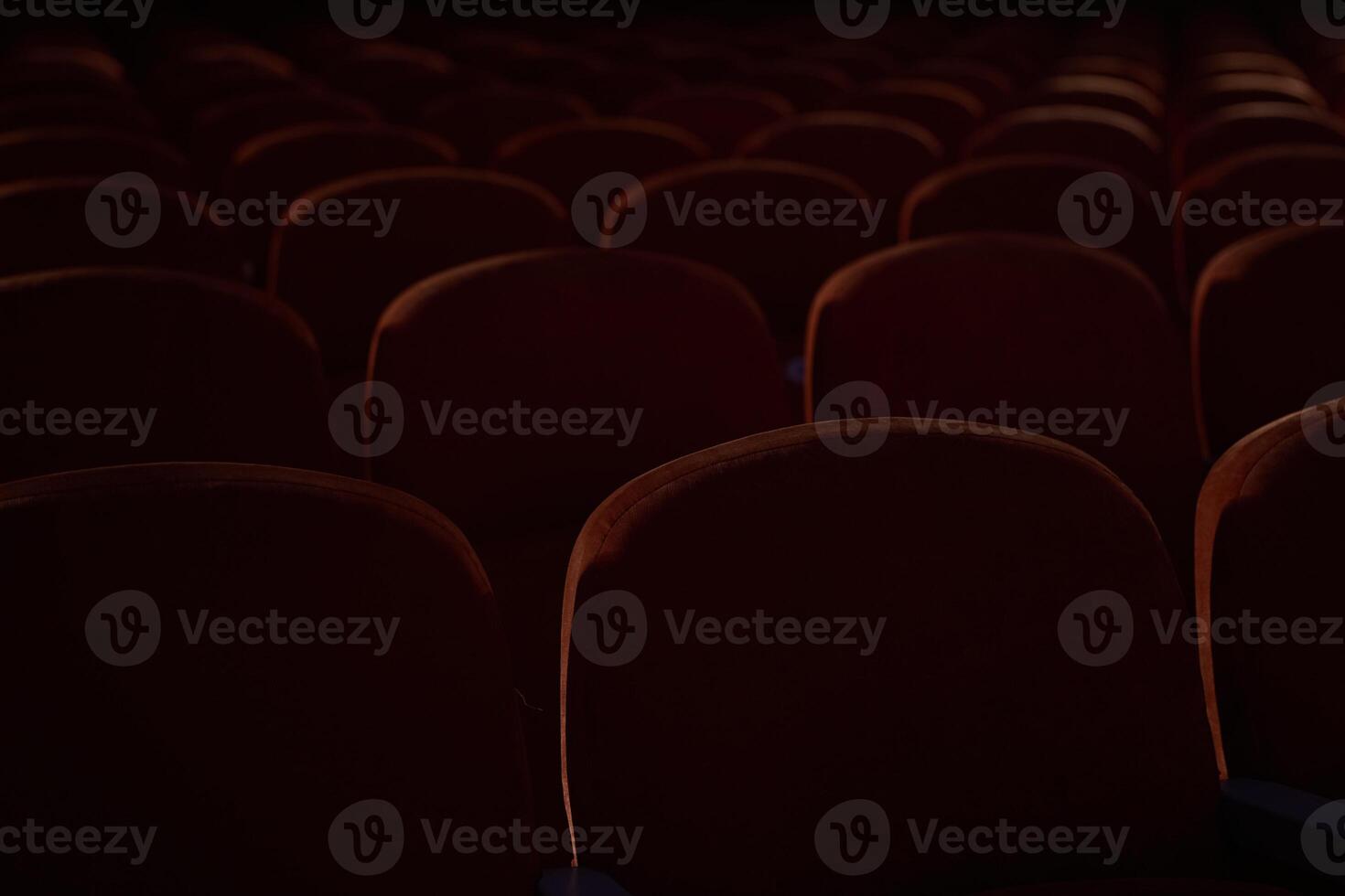 Close up of orange, red seats in dark cinema hall with copy space. Background with rows of chairs with selective focus. Concept of theatre, event, show, presentation, conference, audience photo