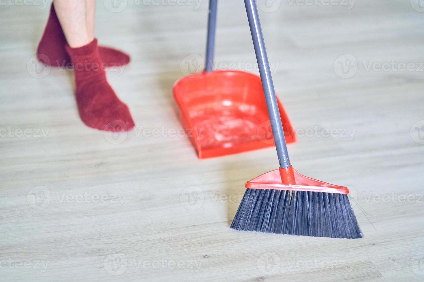 Close up view of a red broom and plastic dustpan on the floor with person's legs in red socks. Worker, cleaner using cleaning items with copy space. Concept of cleaning dust, home and sweeping floor photo