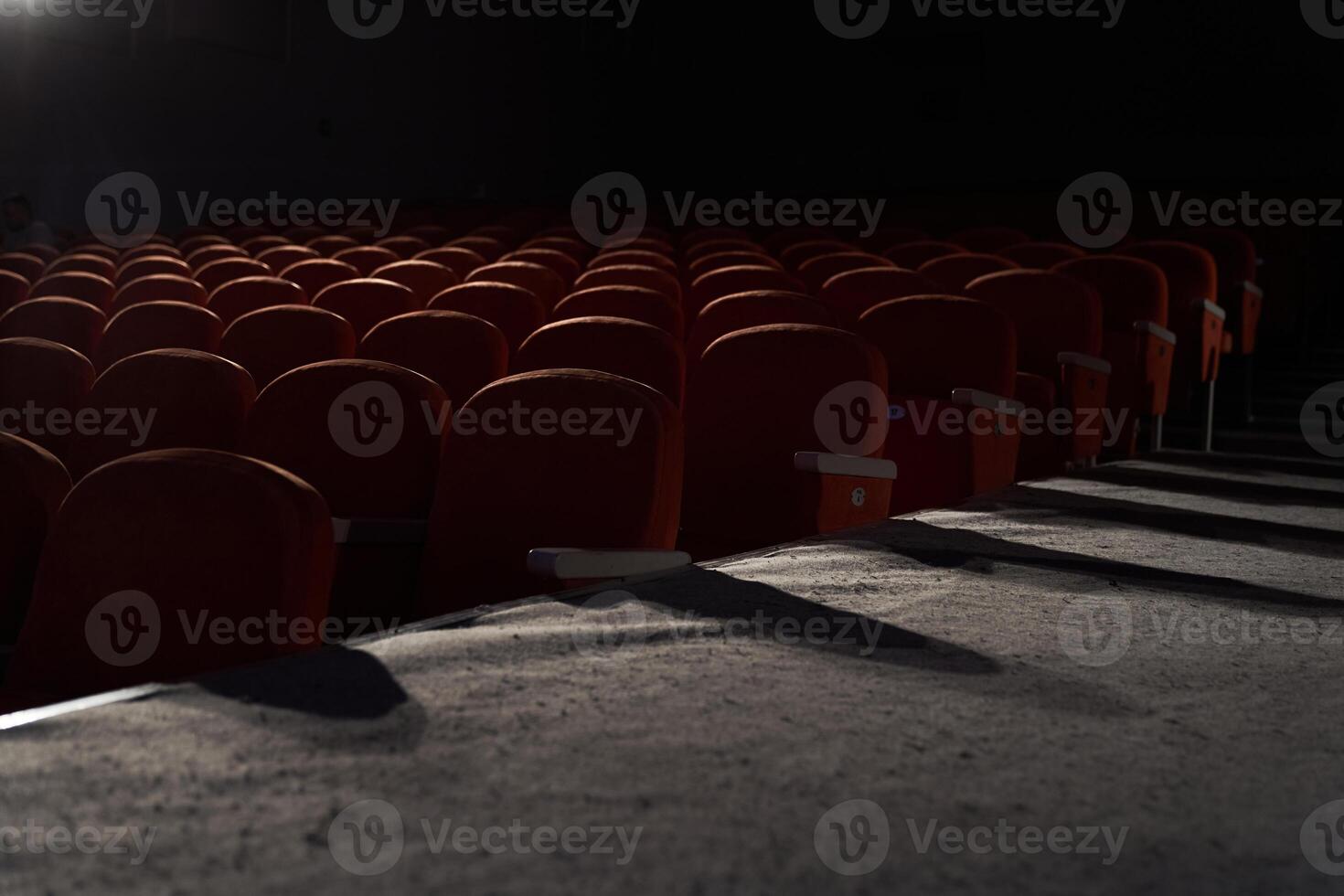 Side view of orange, red seats in dark cinema hall with copy space. Background with rows of chairs with light beam with. Concept of theatre, event, show, presentation, conference, audience photo