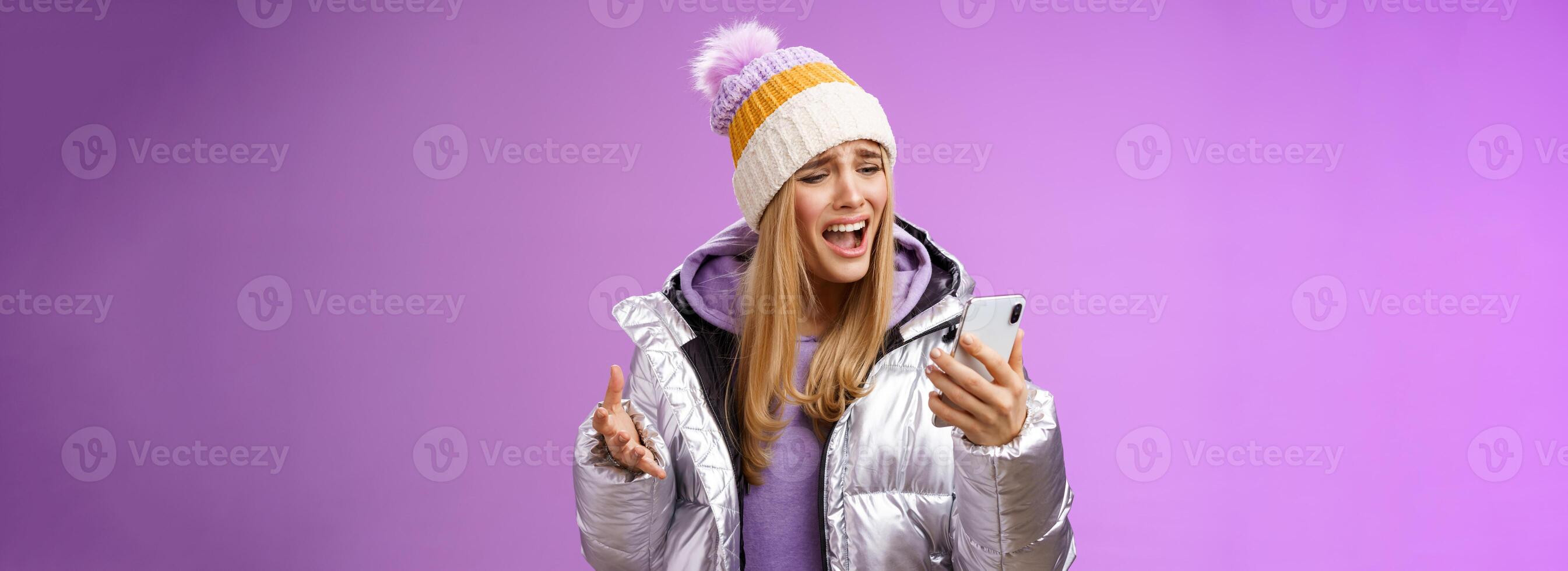 Bothered complaining dissatisfied cute blond girl yelling stupid smartphone standing unhappy recording audio message whining yelling mobile phone upset, standing purple background photo