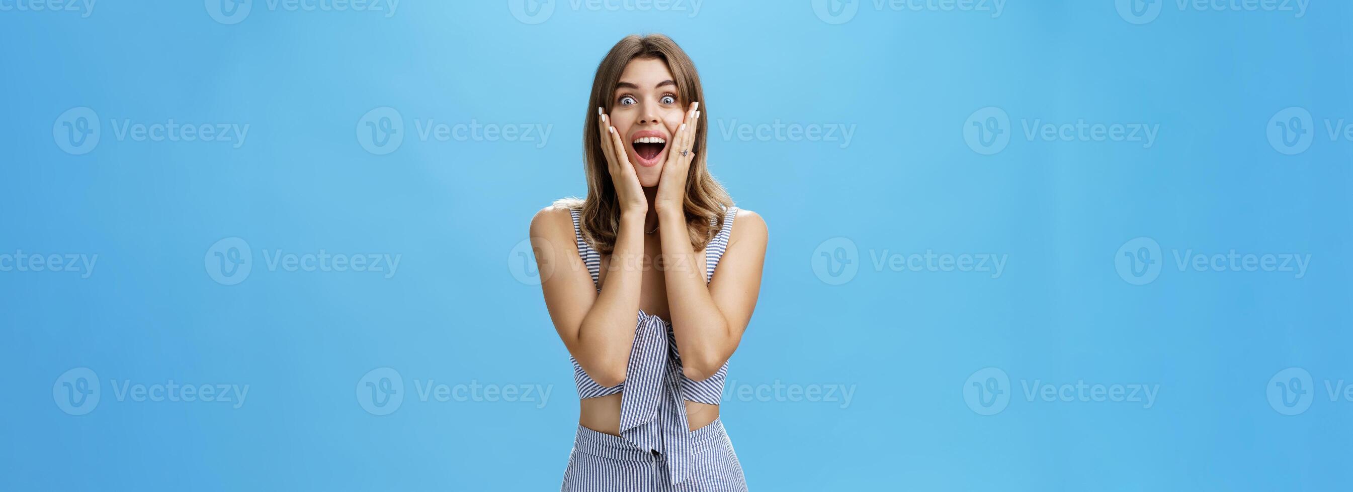 Charismatic surprised good-looking adult european female with cute gap teeth smiling broadly pressing hands to cheeks from amazement and joy gazing delighted and astonished at camera, impressed photo