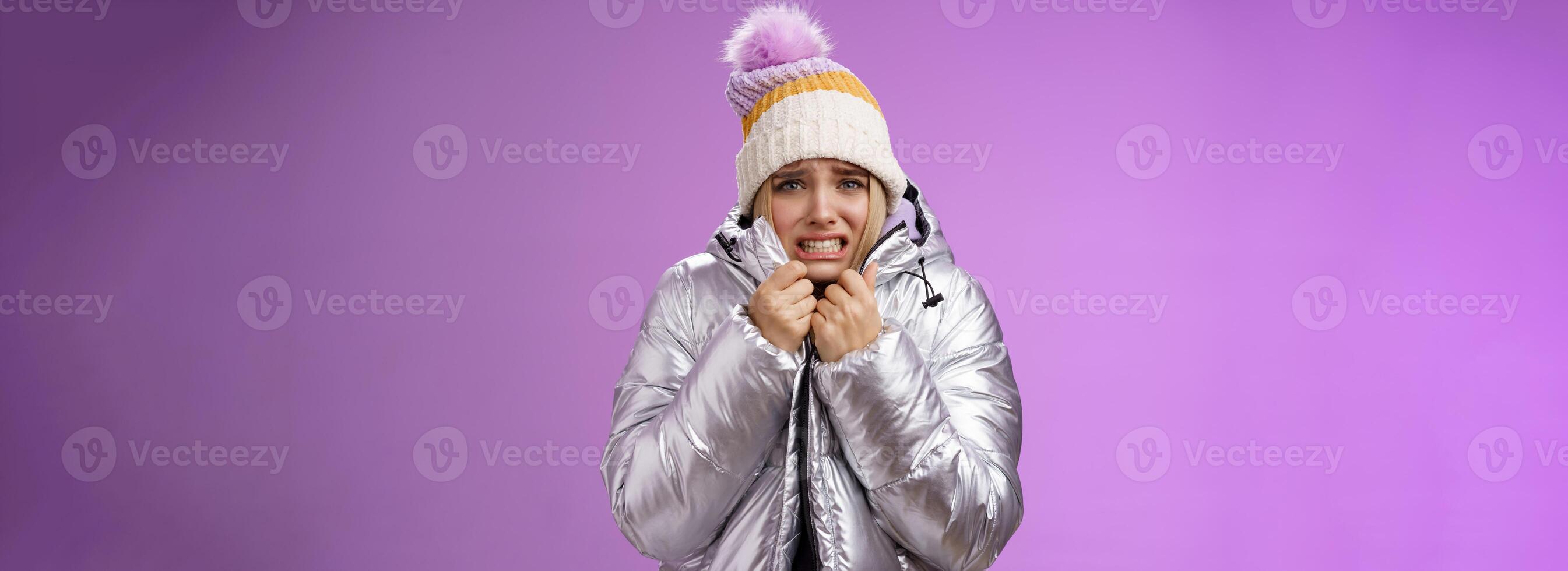 Uncomfortable shaking displeased charming gloomy blond cute woman in silver stylish jacket pulling coat tight wear hat shaking clenching teeth grimacing suffering low temperature freezing cold photo