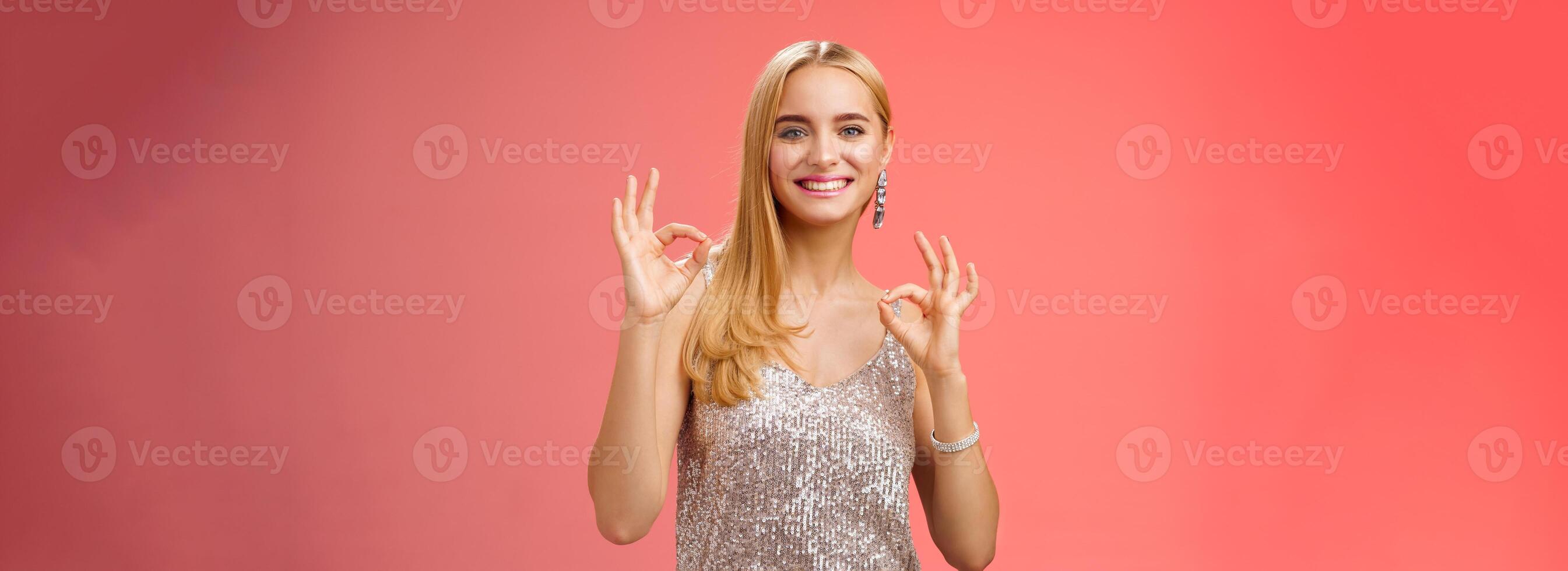 No problem friend. Charming carefree tender blond european woman in silver dress show okay ok gesture smiling pleased recommend awesome party assure having fun, feel excellent red background photo