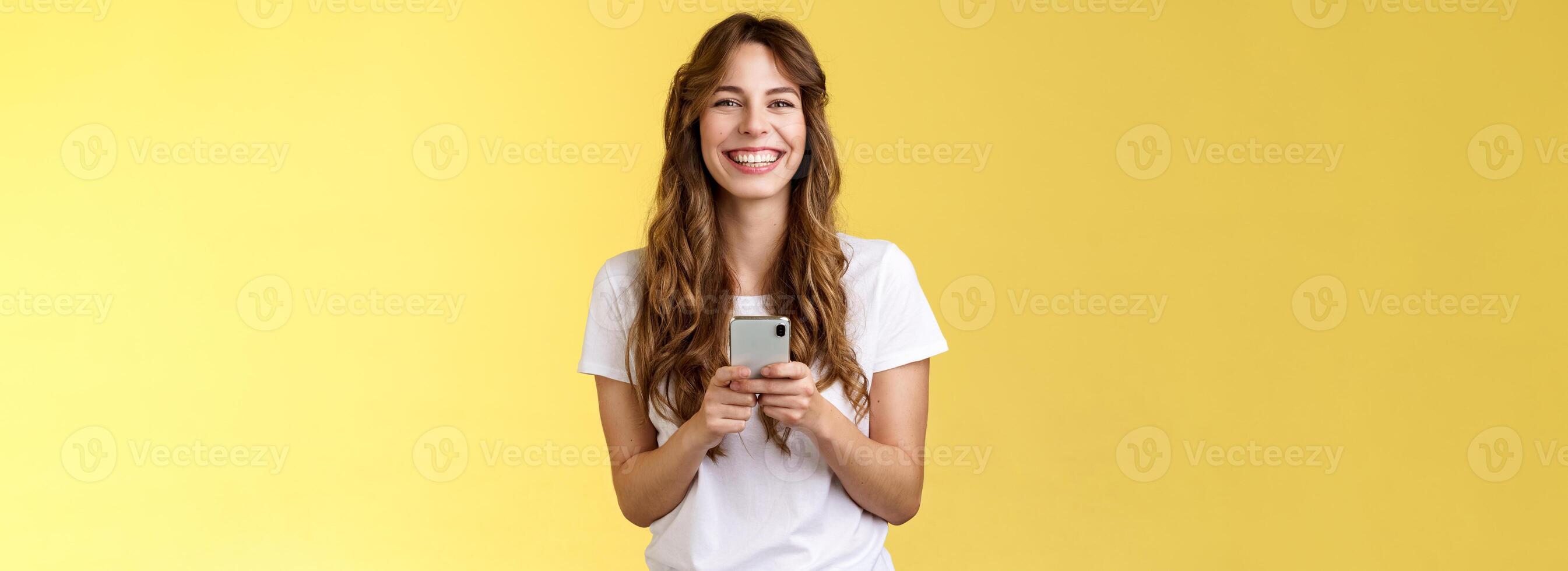 Cheerful carefree happy lively girl hold smartphone using awesome funny app playing cool game relaxing waiting friend park browsing social media using mobile phone look camera upbeat smiling photo