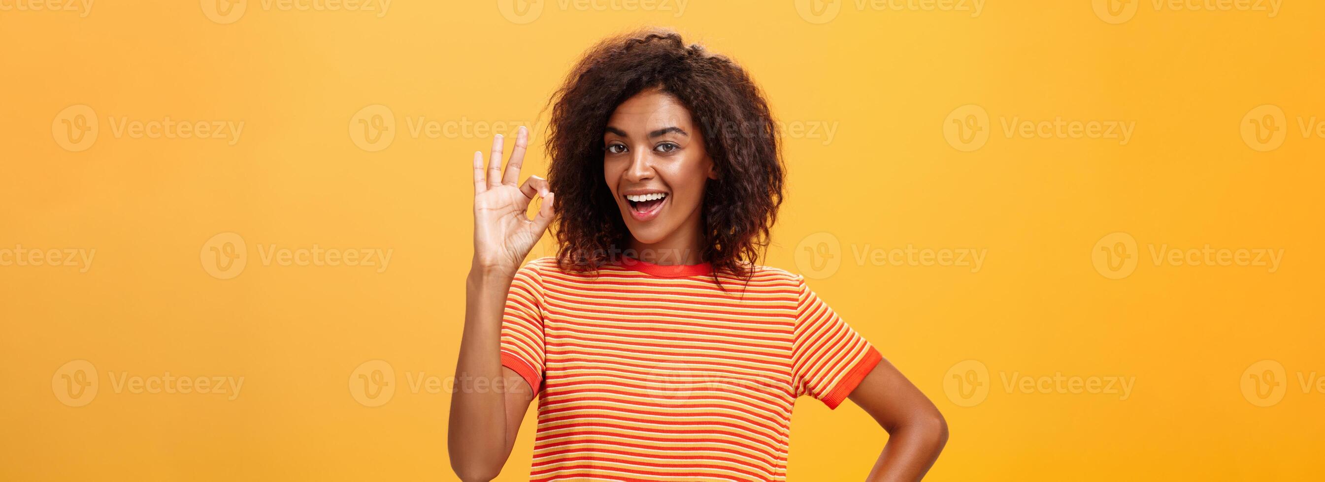 I got it, think it done. Portrait of self-assured good-looking calm and carefree african american woman with curly hairstyle raising ok or excellent gesture and smiling assuring she knows what doing photo