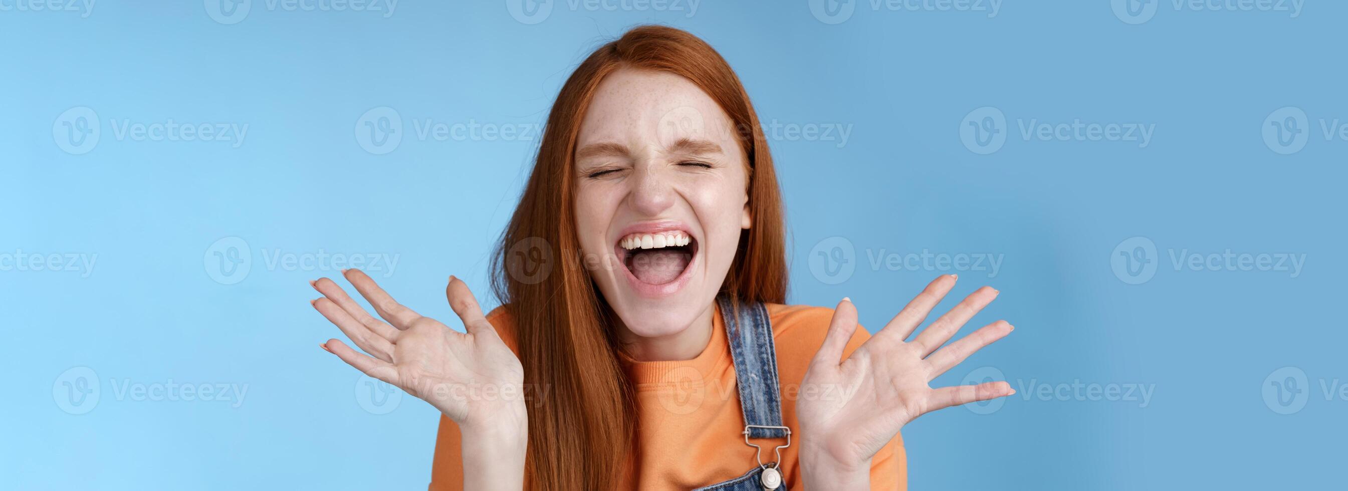 Positive carefree triumphing young attractive redhead girl scream out loud joy happiness close eyes waving raised hands win first prize dream come true celebrating victory good news, blue background photo
