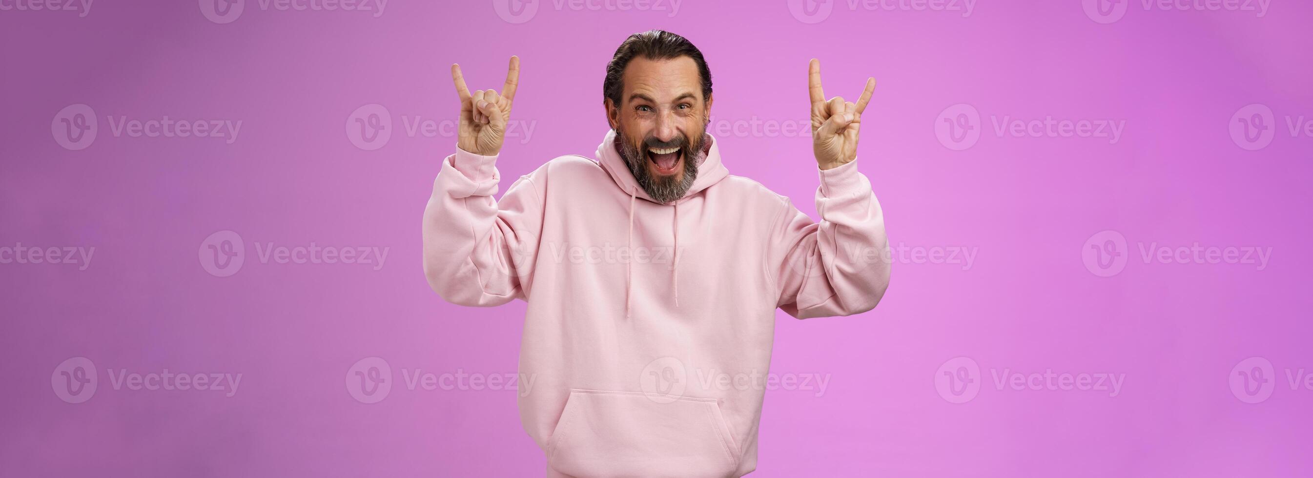 Carefree enthusiastic excited mature bearded man grey hair having fun show rock-n-roll gesture attend awesome heavy metal concert grimacing thrilled looking happy upbeat, purple background photo
