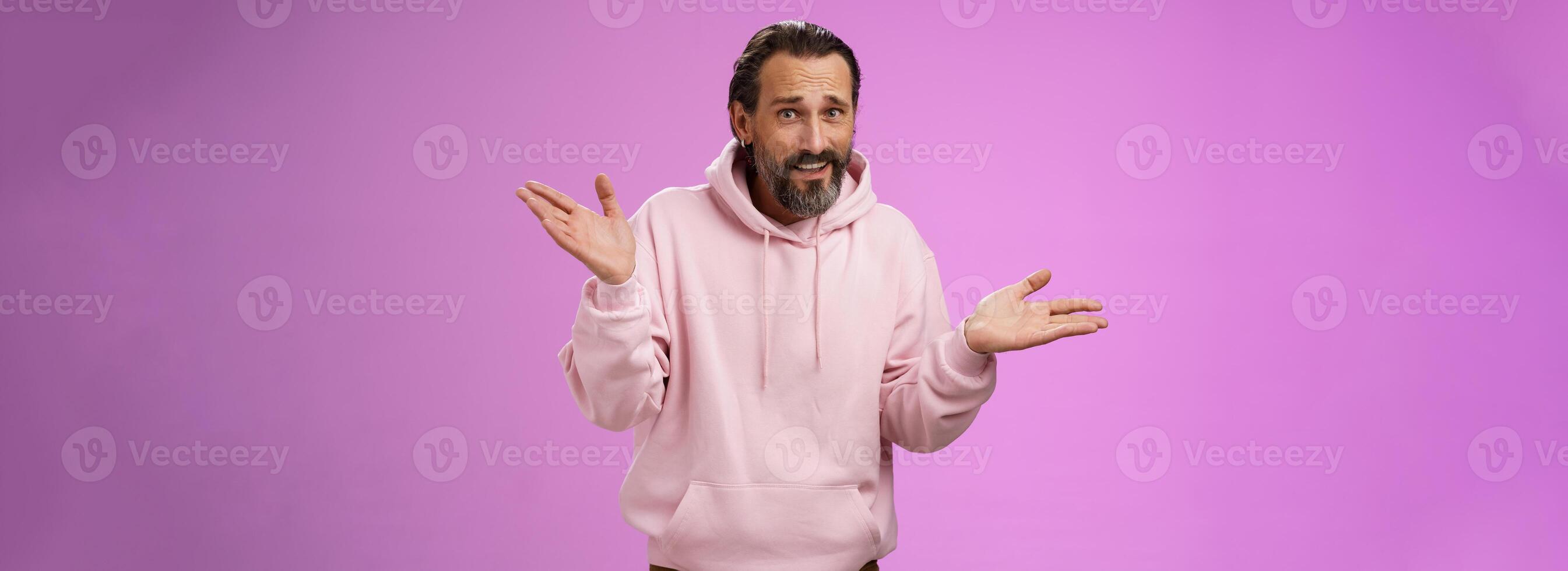 So what bite me. Portrait ignorant careless cool stylish mature bearded man earring pink hoodie shrugging hands sideways mocking being rude standing pissed unwilling help standing purple background photo