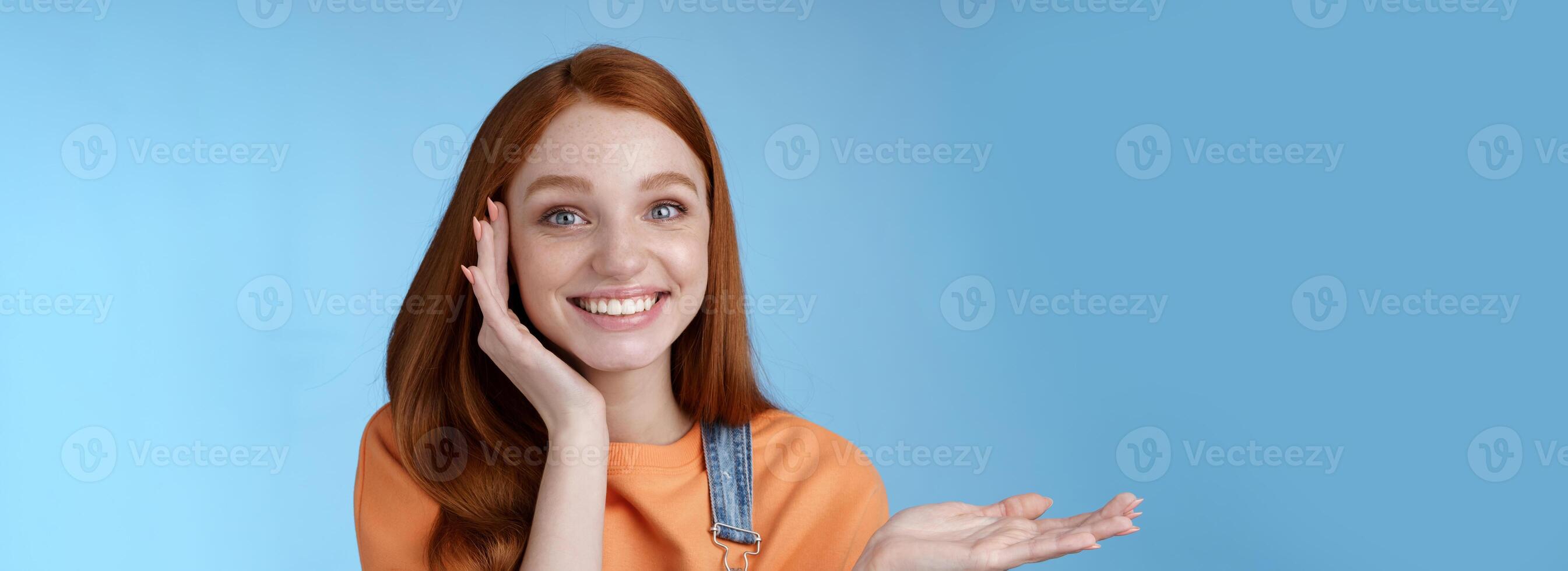 Cute tender chatismatic glad smiling redhead girl presenting awesome product show object palm hold hand raised blank copy space grinning impressed receive silly charming gift, blue background photo