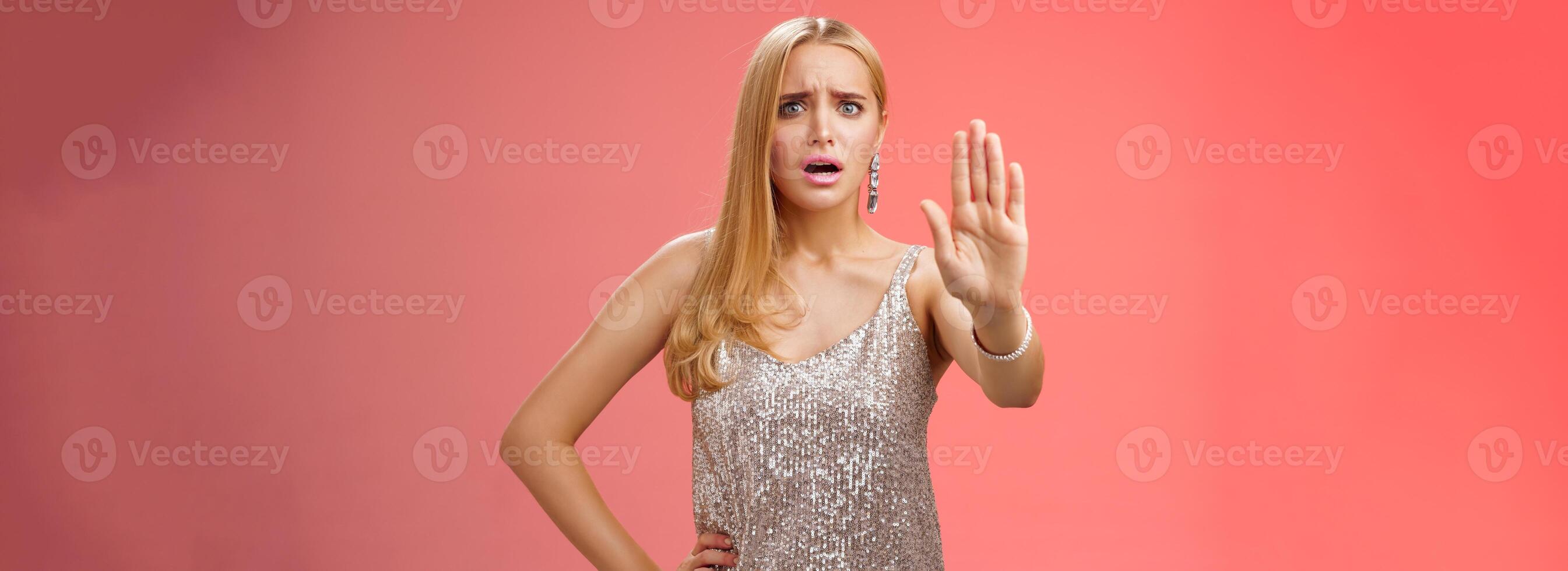 Freaked out displeased bothered insecure blond woman in silver glittering dress extend palm stop enough prohibition rejection gesture bothered pissed annoying clingy man nightclub, red background photo