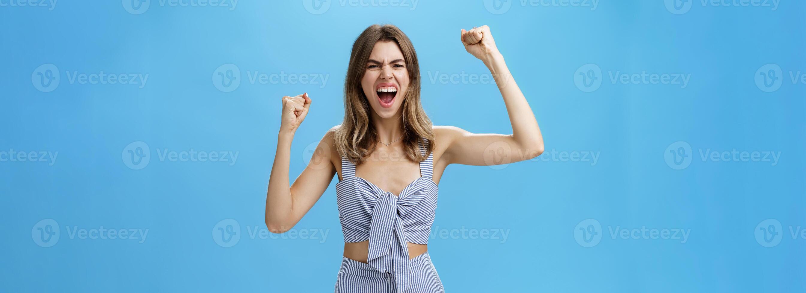 Excited and thrilled overwhelmed attractive woman in matching stylish clothes becoming fan of football standing on stadium yelling to cheer team raising clenched fists in rage and victory gesture photo