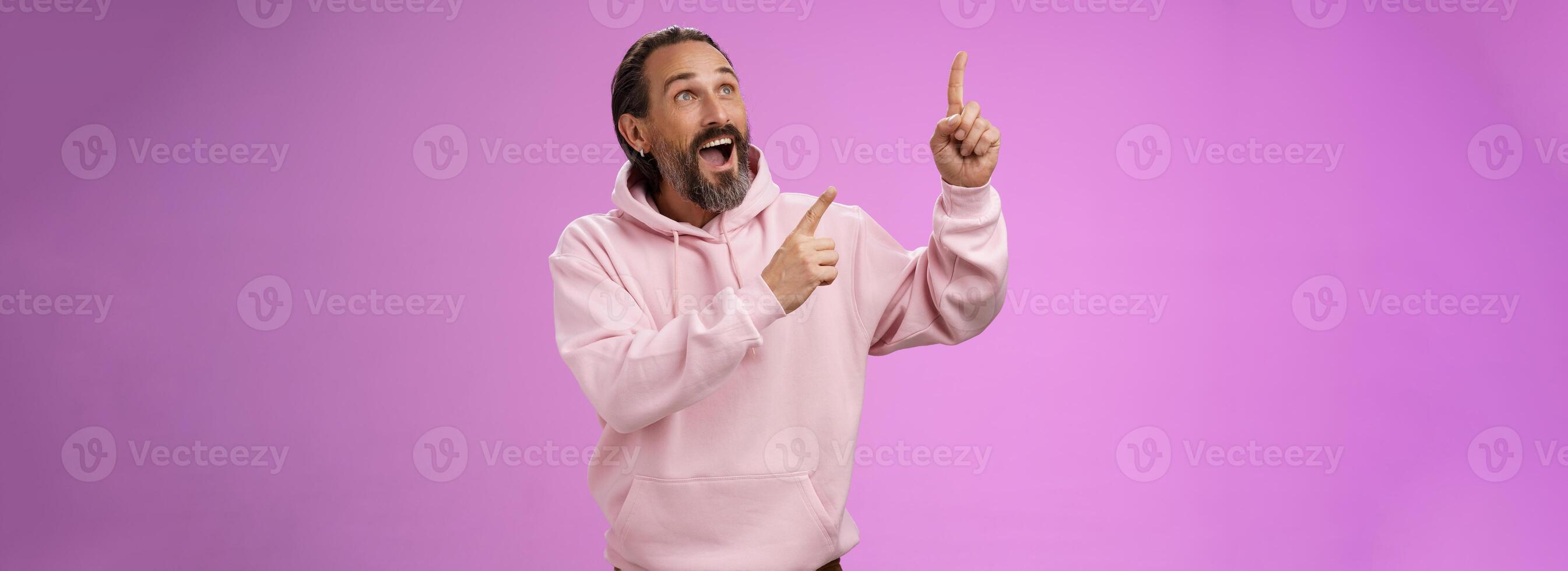 Fashionable good-looking fascinated mature bearded man grey hair look astonished pointing gazing upper left corner see miracle incredible breathtaking magnificanent view, standing purple background photo