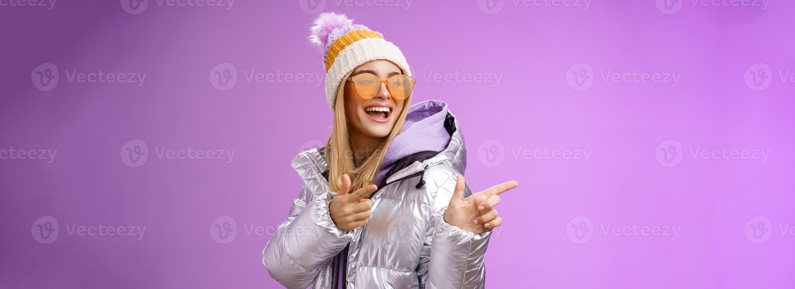 Hey how you doin. Cheeky stylish bond girl having fun greeting friend pointing finger pistols left smiling sassy say hello what up wearing cool silver jacket hat sunglasses, purple background photo