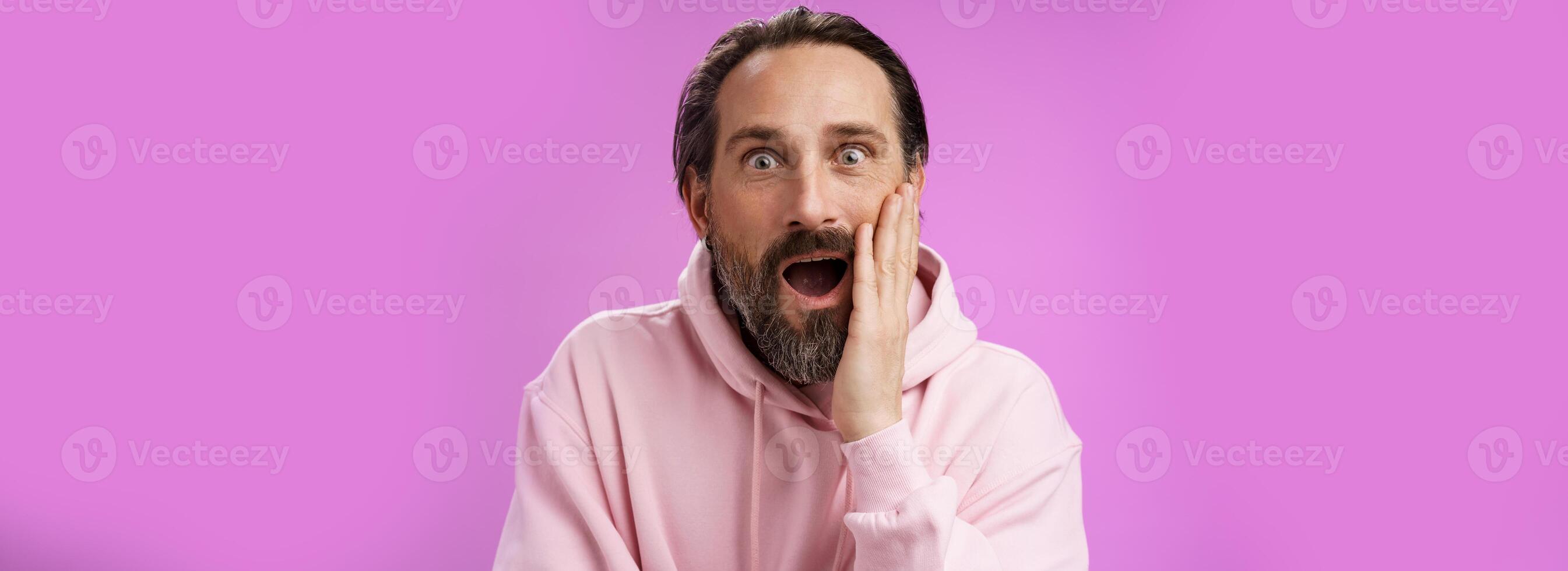 Impressed fascinated speechless mature male attend interesting lecture drop jaw thrilled touch cheek palm widen eyes surpised astonished, standing purple background amzed and amused photo