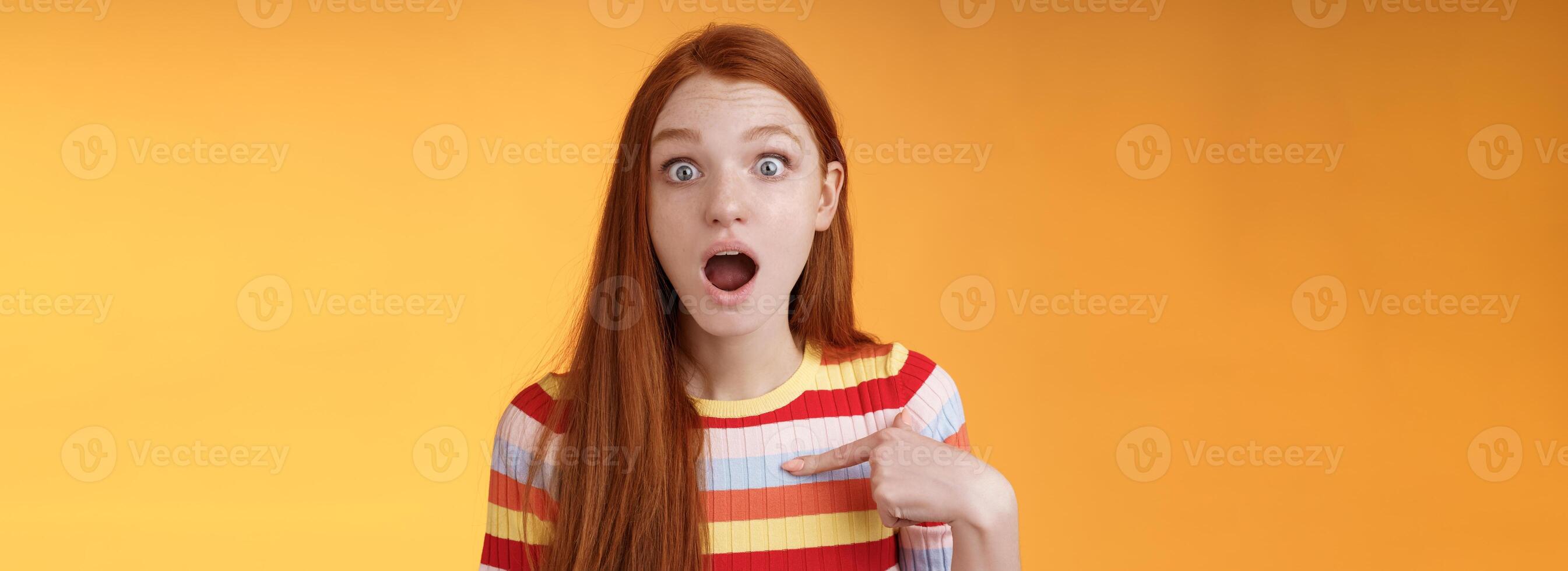 Shocked silly surprised redhead cute girl gasping drop jaw stunned stare camera full disbelief pointing herself cannot believe chosen picked participate event standing impressed orange background photo