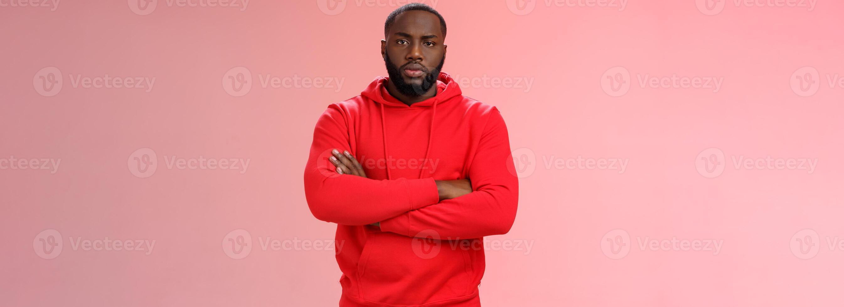 Serious-looking strong black guy security worker cross hands chest confident bossy pose frowning making solid scary look wearing red hooide posing red background, employer controling work photo