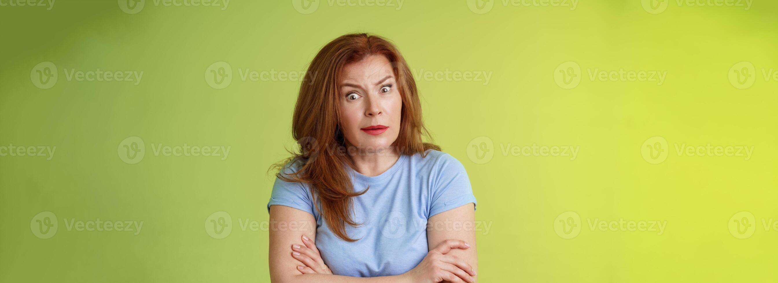 You did what. Confused shocked speechless redhead mature mother stare camera puzzled concerned cross arms chest self-soothing bothered pose look questioned hesitant green background photo