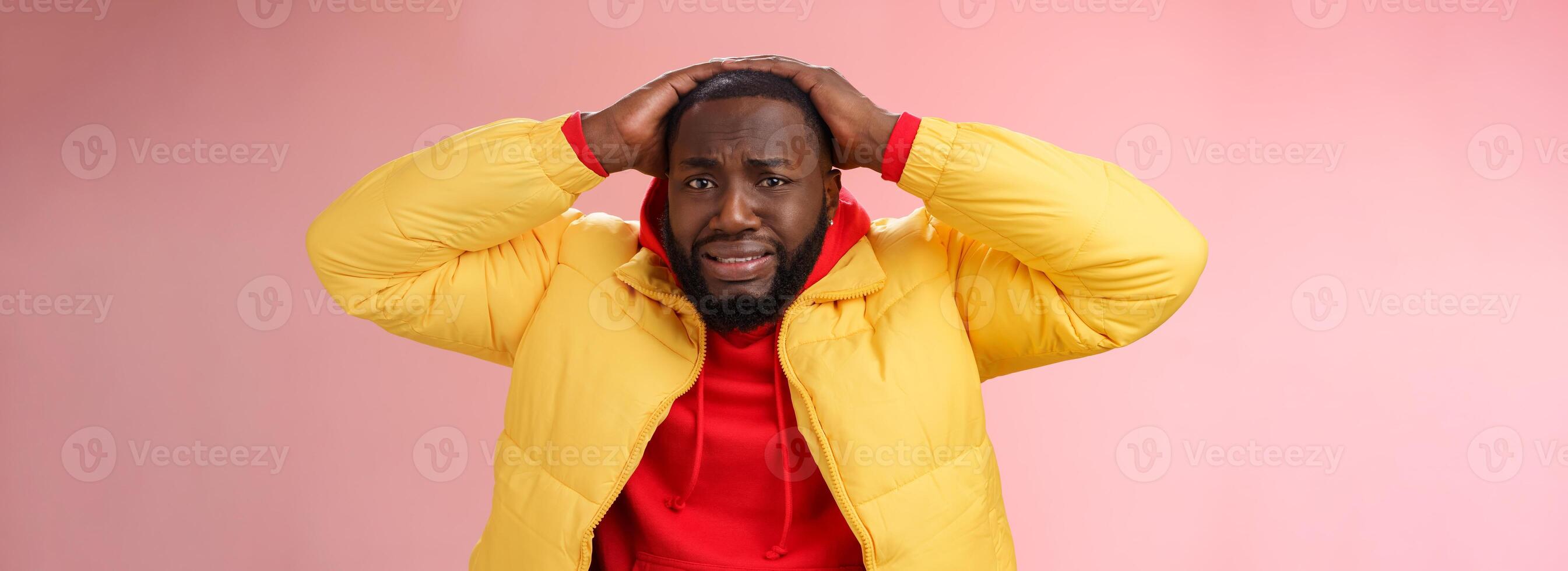 Troubled shocked young upset male coworker feel bad anxiously cringing holding hands head frowning losing bet lottery standing sorrow unhappy pink background wear yellow coat photo