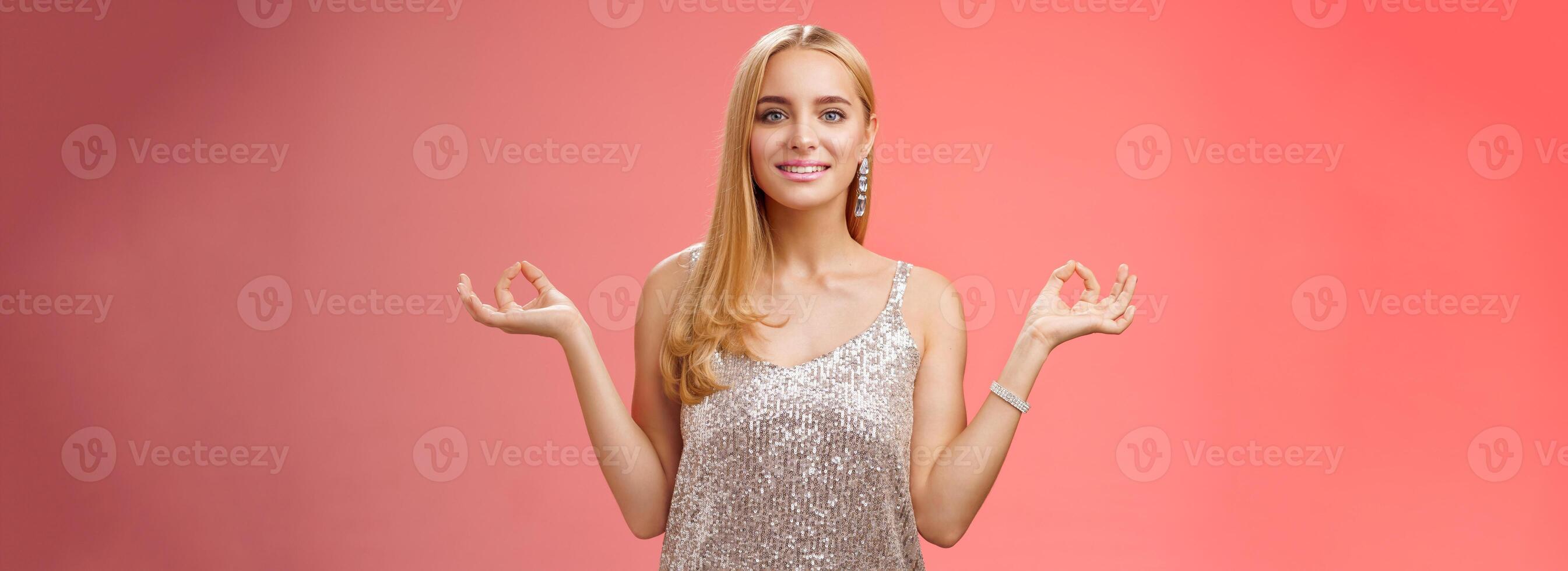 Calm relieved happy fabulous young blond woman in silver stylish luxury dress standing relaxed red background zen lotus pose reach nirvana smiling peaceful carefree meditating breathing practice photo