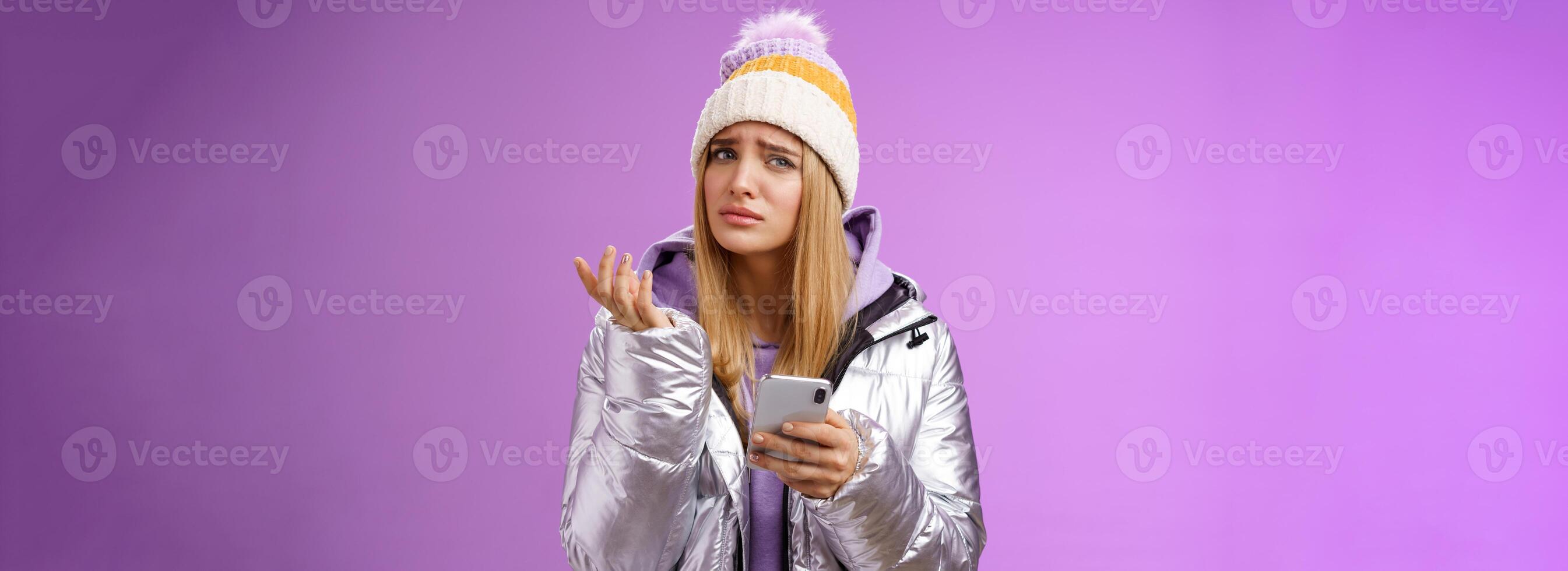 Questioned complicated cute blond girlfriend receive strange message look perplexed confused raising hand shrugging lift eyebrow cannot understand meaning holding smartphone, purple background photo