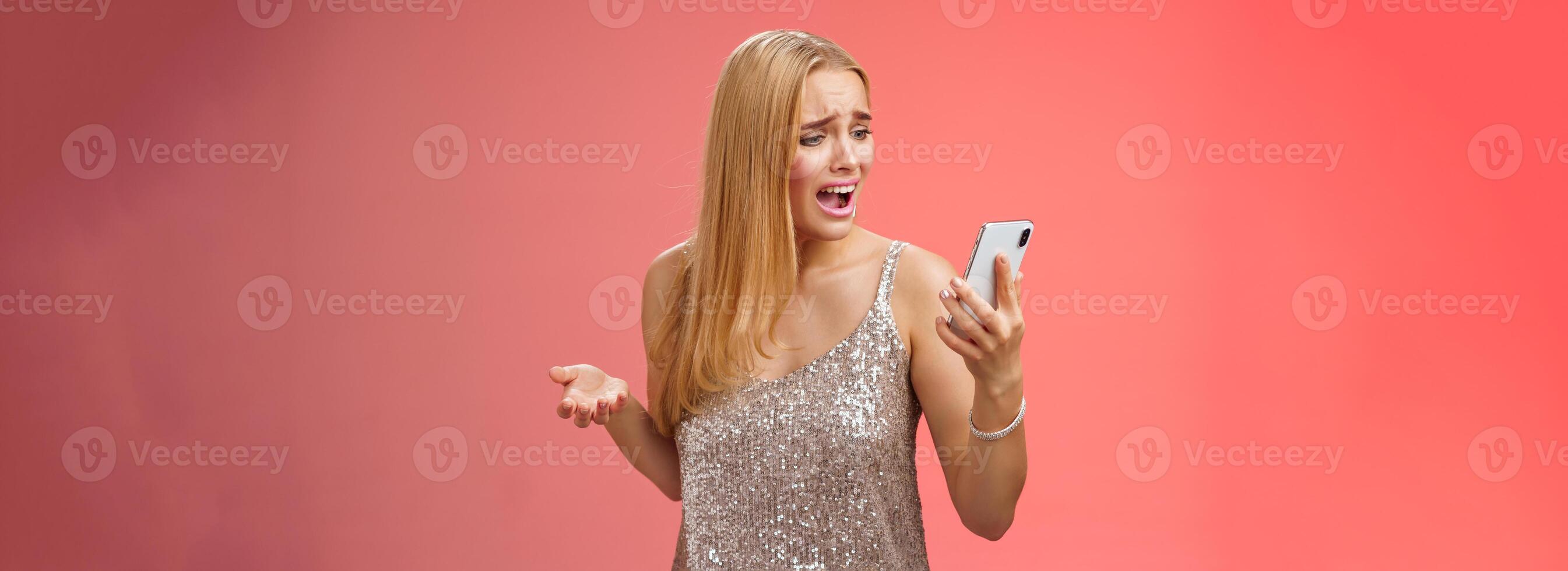 Troubled concerned arrogant young blond woman complaining yelling smartphone cannot call friend no signal holding smartphone look mobile display pissed moody arguging, red background photo
