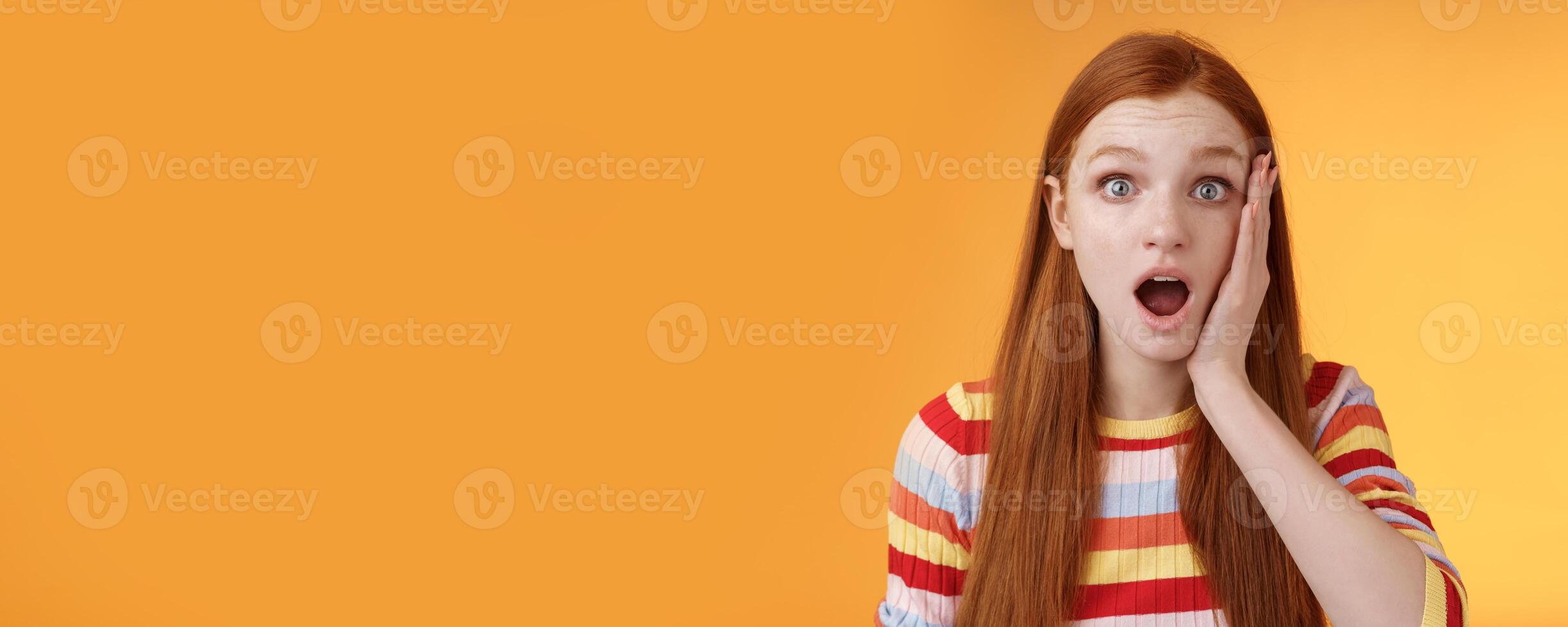 Shocked impressed concerned ginger girl drop jaw gasping stunned slap cheek wide eyes surprised hear disturbing terrible news standing orange background sympathizing awful story photo