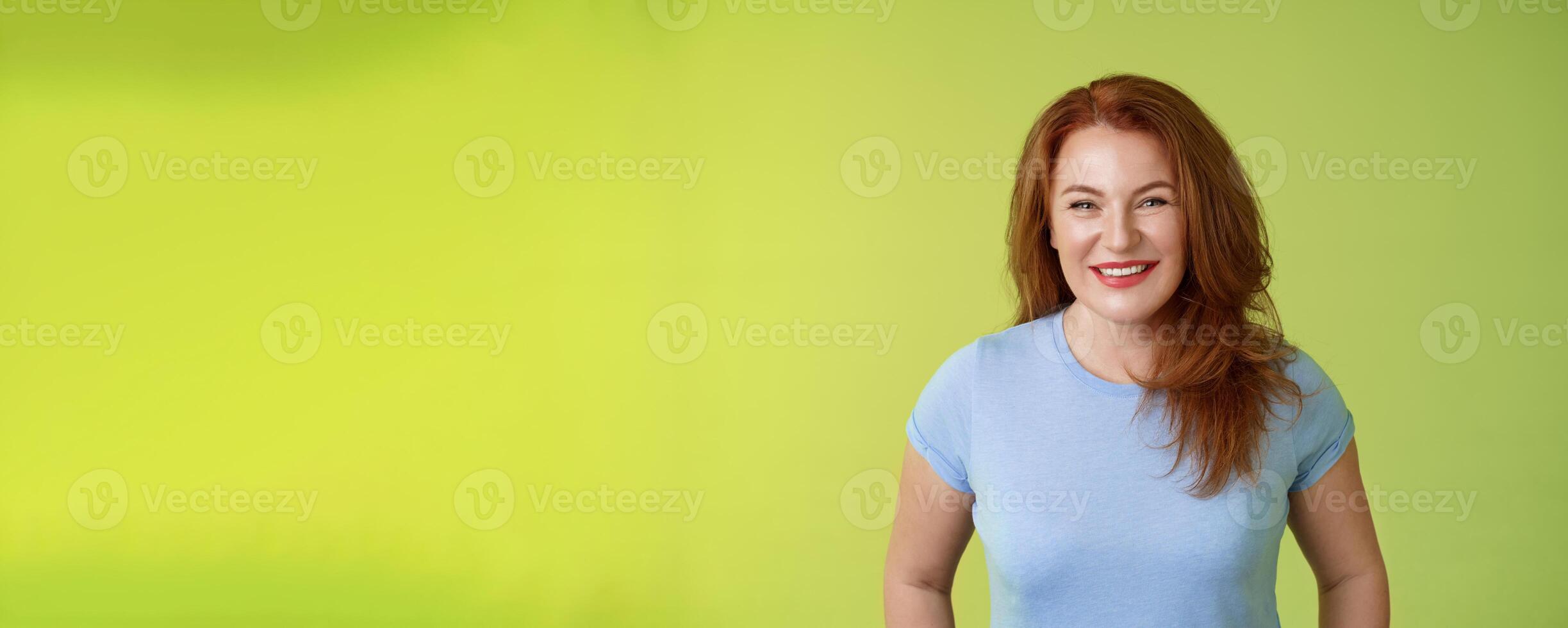 Cheerful kind happy redhead middle-aged mother look caring delighted smiling broadly gaze admiration joy stand blue t-shirt green background amused enthusiastic expression photo