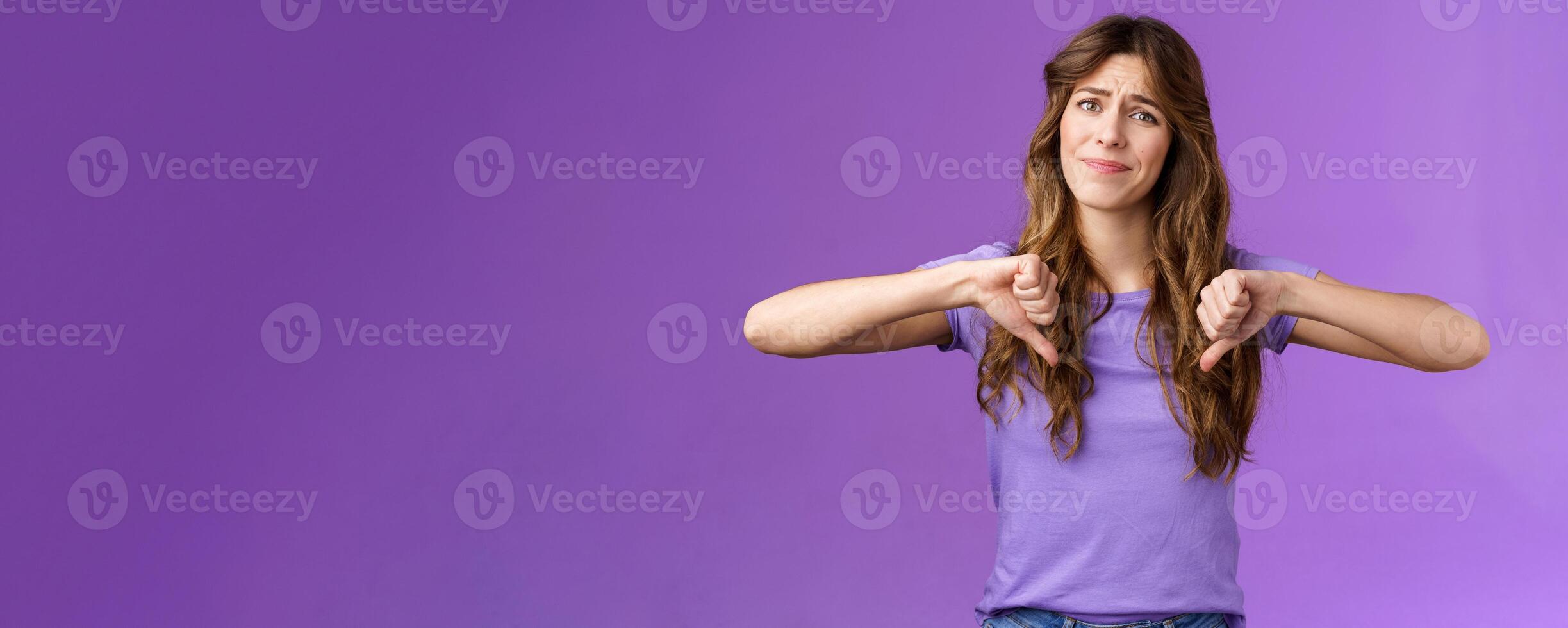 Disappointed displeased pity girl show thumbs down grimace dislike express negative opinion thumbs down gesture apologizing giving bad feedback stand purple background unimpressed photo