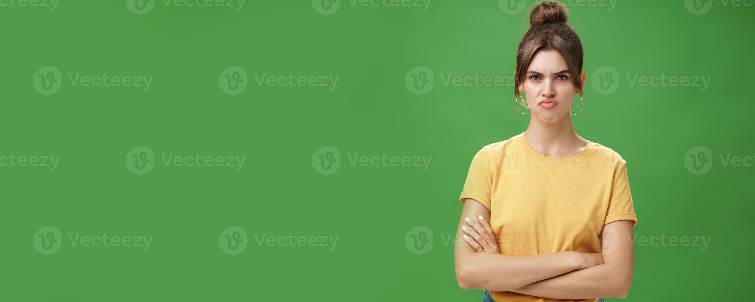 Girl not liking result of work looking displeased and serious at camera, frowning crossing hands against chest, pursing lips from disappointment, being offended over green background photo