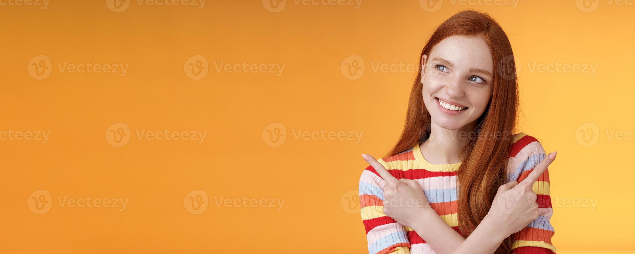 Dreamy cute redhead girl planning were go summer holidays have different choices picking variant look intrigued smiling pleased pointing sideways left right taking decision, orange background photo