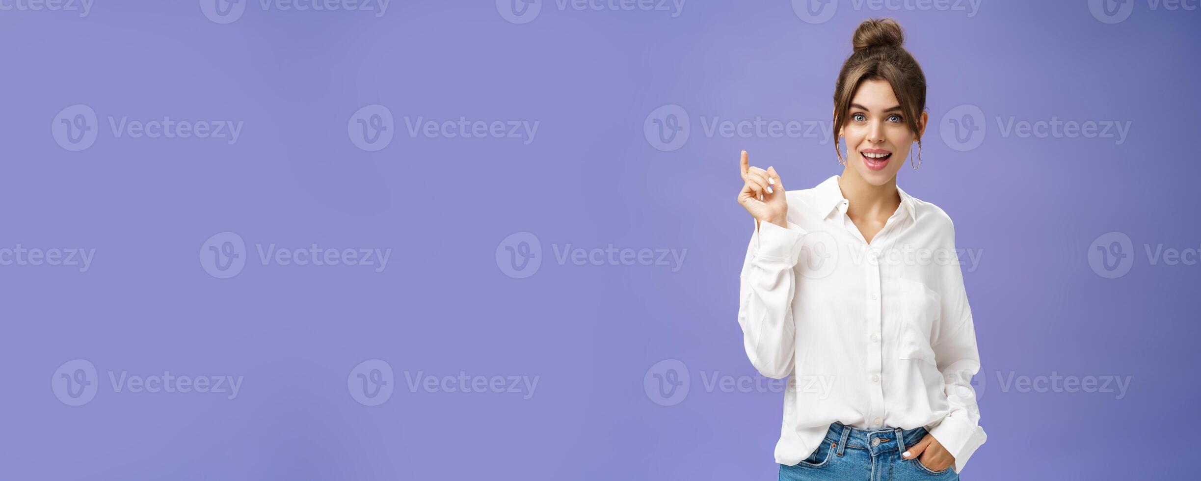 Expressive charismatic and beautiful white girl with combed hair in stylish white blouse holding hand in pocket gesturing during talk and smiling at camera with friendly gaze over purple wall photo