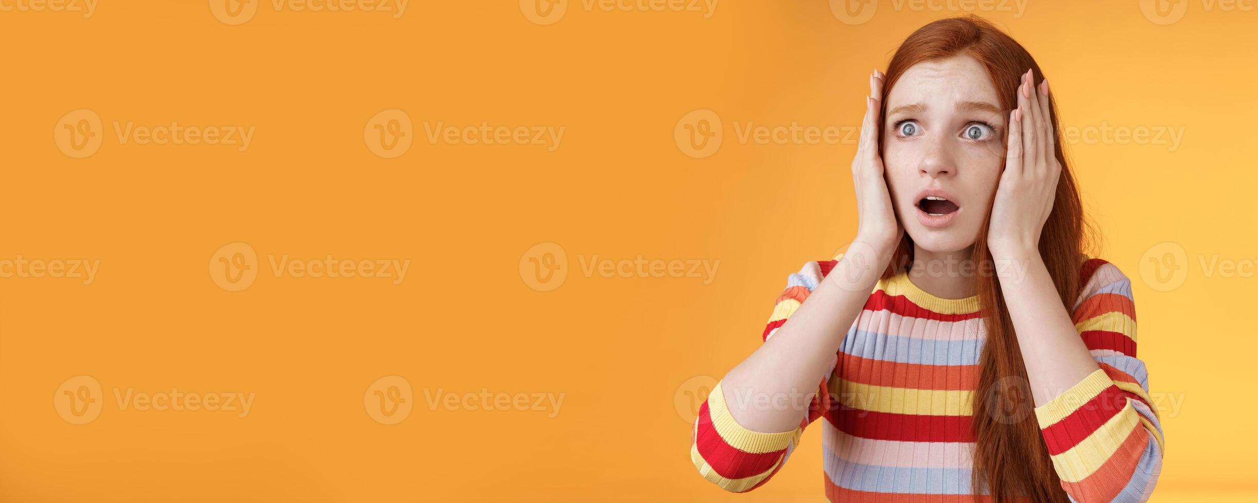 Worry insecure redhead european panicking girl grab head hands both sides gasping open mouth shocked stare frightened upset watching terrible accident standing concerned orange background photo