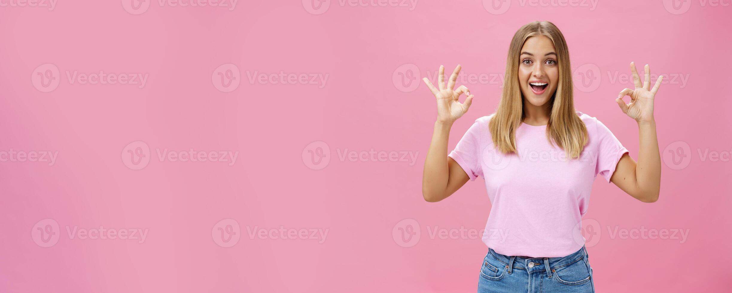 Portrait of enthusiastic attractive caucasian girl in trendy t-shirt and jeans showing okay or confirm gesture with amused broad smile standing pleased over pink background reacting to excellent news photo