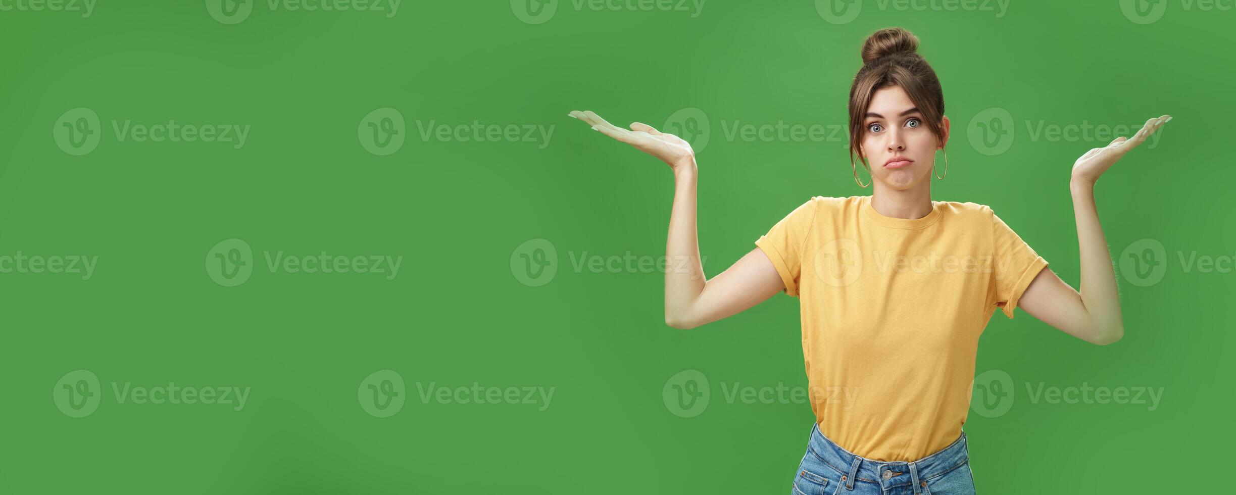 Girl do not know anything. Portrait of confused unsure cute woman with combed hair shrugging with raised hands pouting looking clueless at camera standing questioned against green background photo
