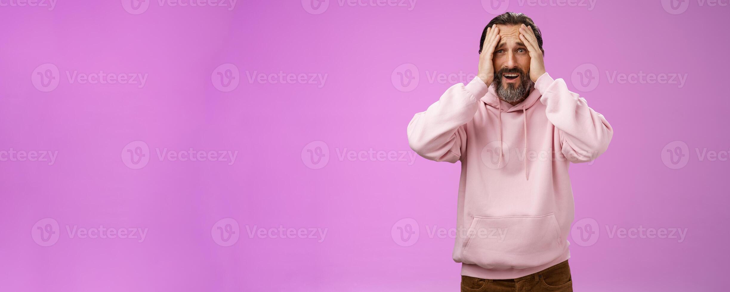Adult upset bearded man despair standing troubled concerned touching face frowning grimacing sorrow unhappiness, losing bet, was robbed, standing shocked devastated purple background, panic photo