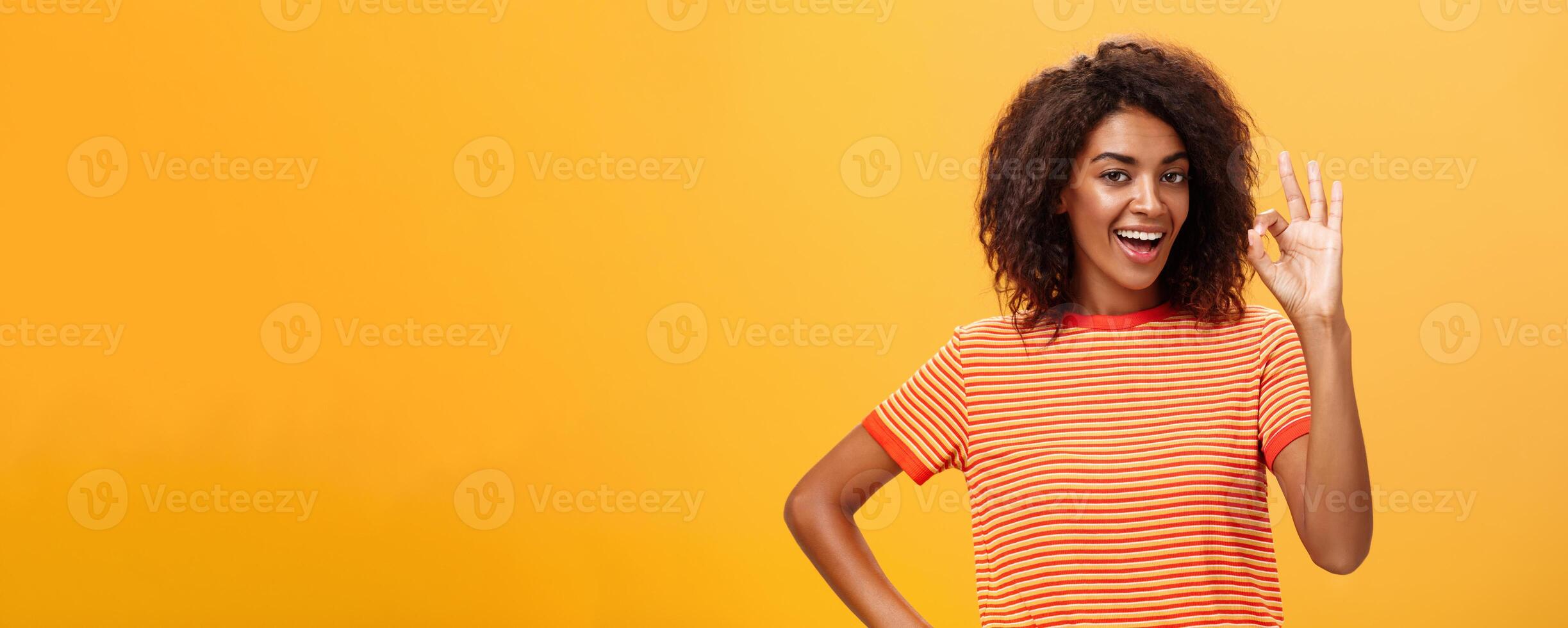 I got it, think it done. Portrait of self-assured good-looking calm and carefree african american woman with curly hairstyle raising ok or excellent gesture and smiling assuring she knows what doing photo